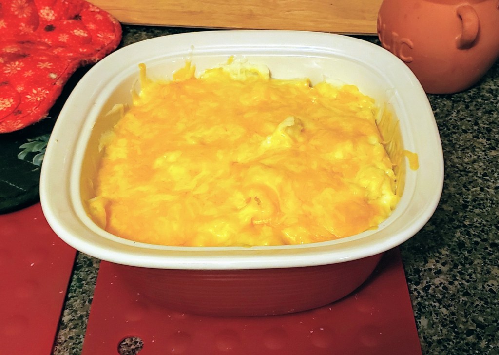 A red casserole dish with mashed potatoes covered in cheddar-jack cheese