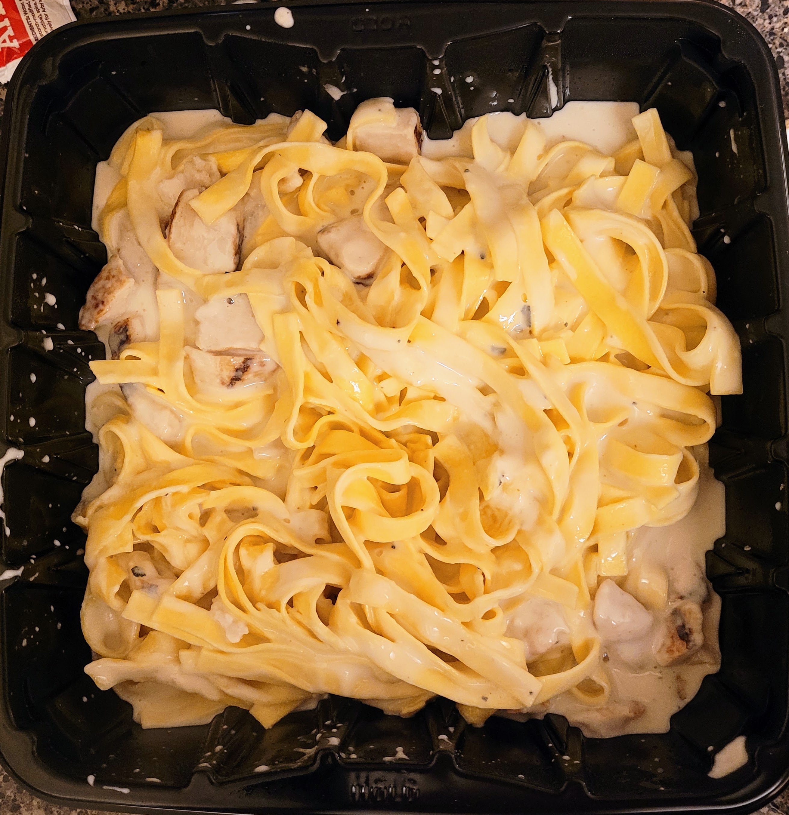 Square black container with egg noodles and cream sauce